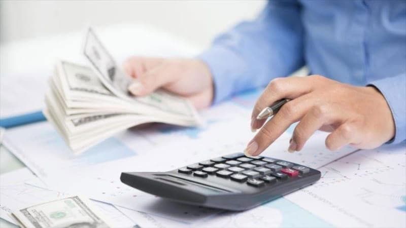 Người làm việc với máy tính cầm tay, tiền và tài liệu tài chính